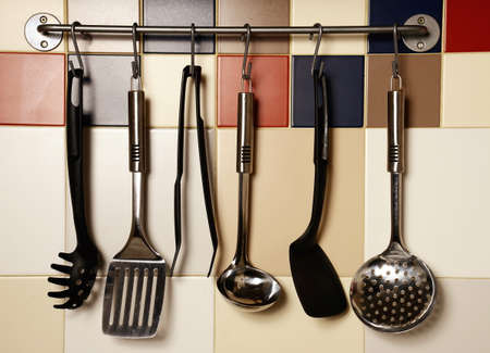 54898080-kitchen-utensils-hanging-on-a-colored-tile-wall.jpg